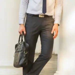 Man wearing a slim-fit white formal shirt, dark grey tailored trousers, and a navy blue tie, holding a black leather briefcase, exuding a professional and polished look suitable for office wear or formal occasions.